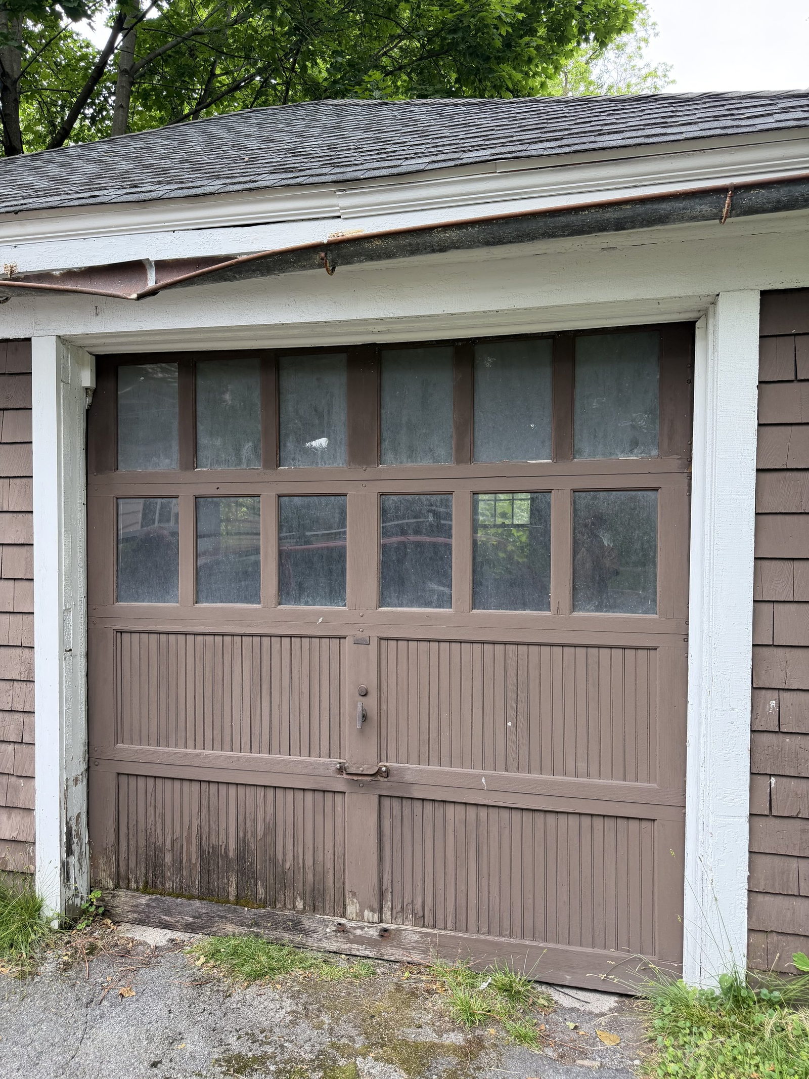 Brown carriage-style wood garage door with a row of glass panes on a detached single-car garage.