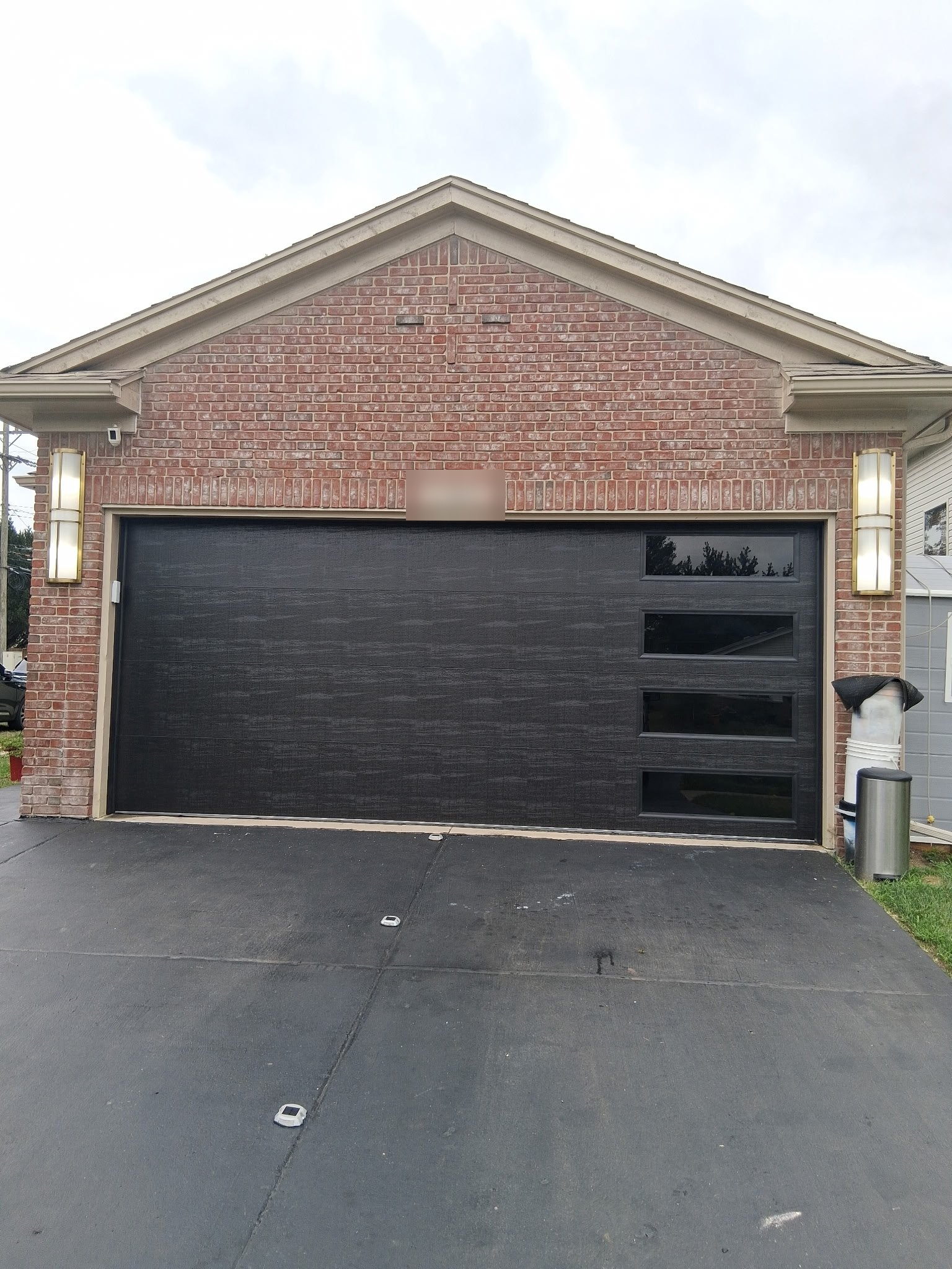 Black flush-panel double garage door with a vertical row of windows on a brick home.