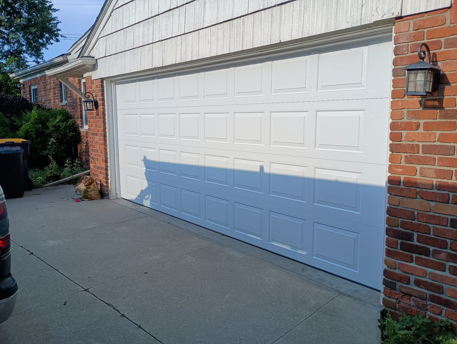 White raised-panel double garage door on a brick and siding home, closed, with a concrete driveway.