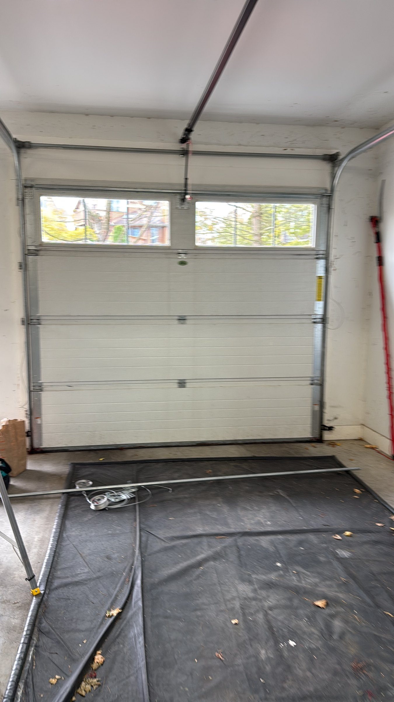 White insulated sectional garage door with a windowed top section, seen from inside an empty garage.