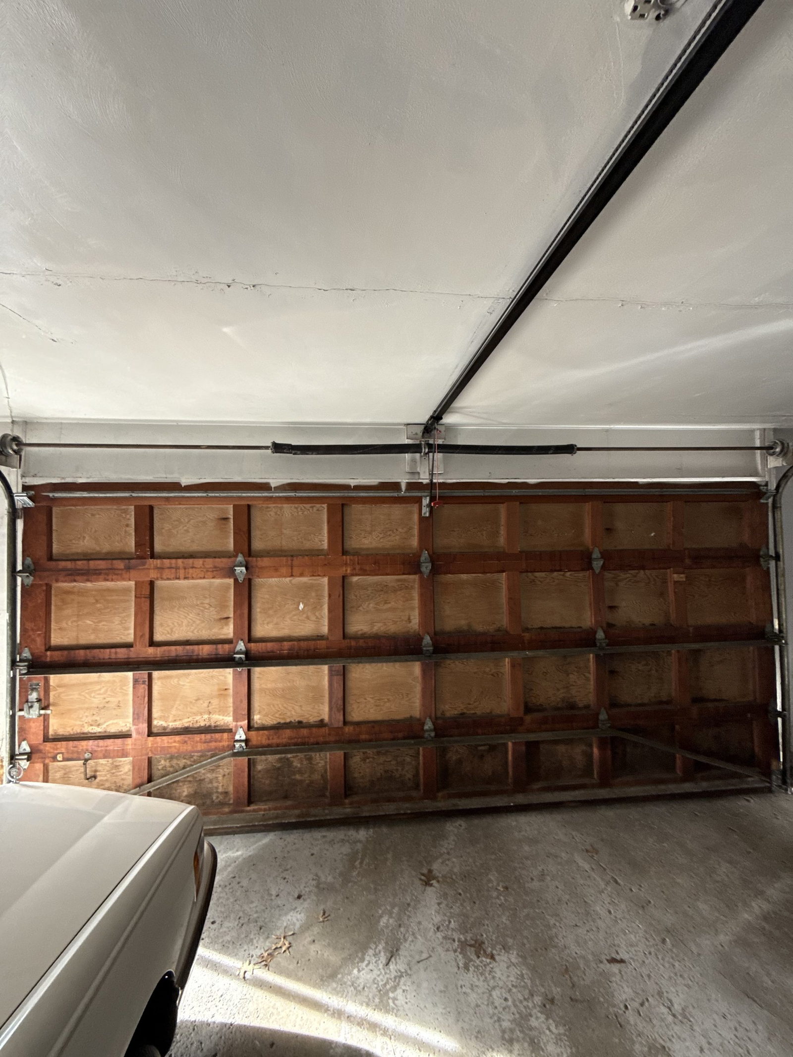 Older wood-panel double garage door seen from inside, with the torsion shaft and track above it.