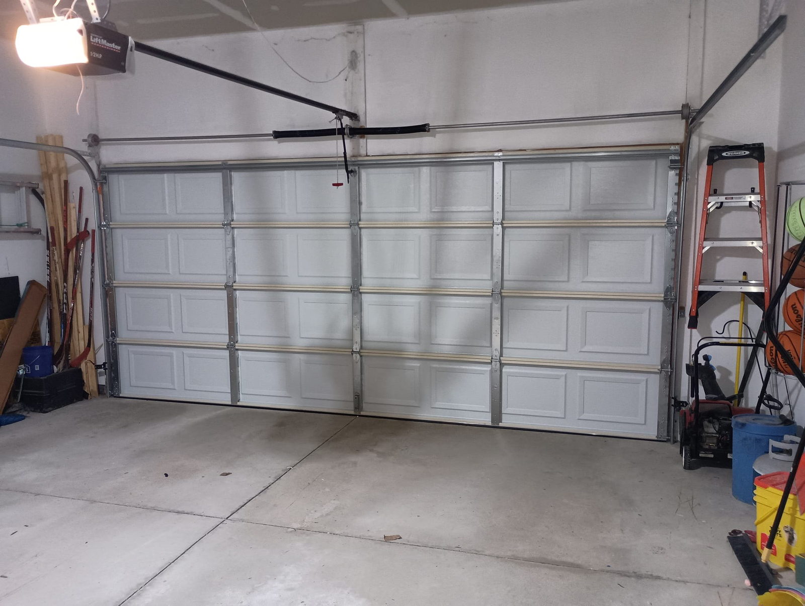 Closed white raised-panel double garage door seen from inside, with the opener rail running to the motor.
