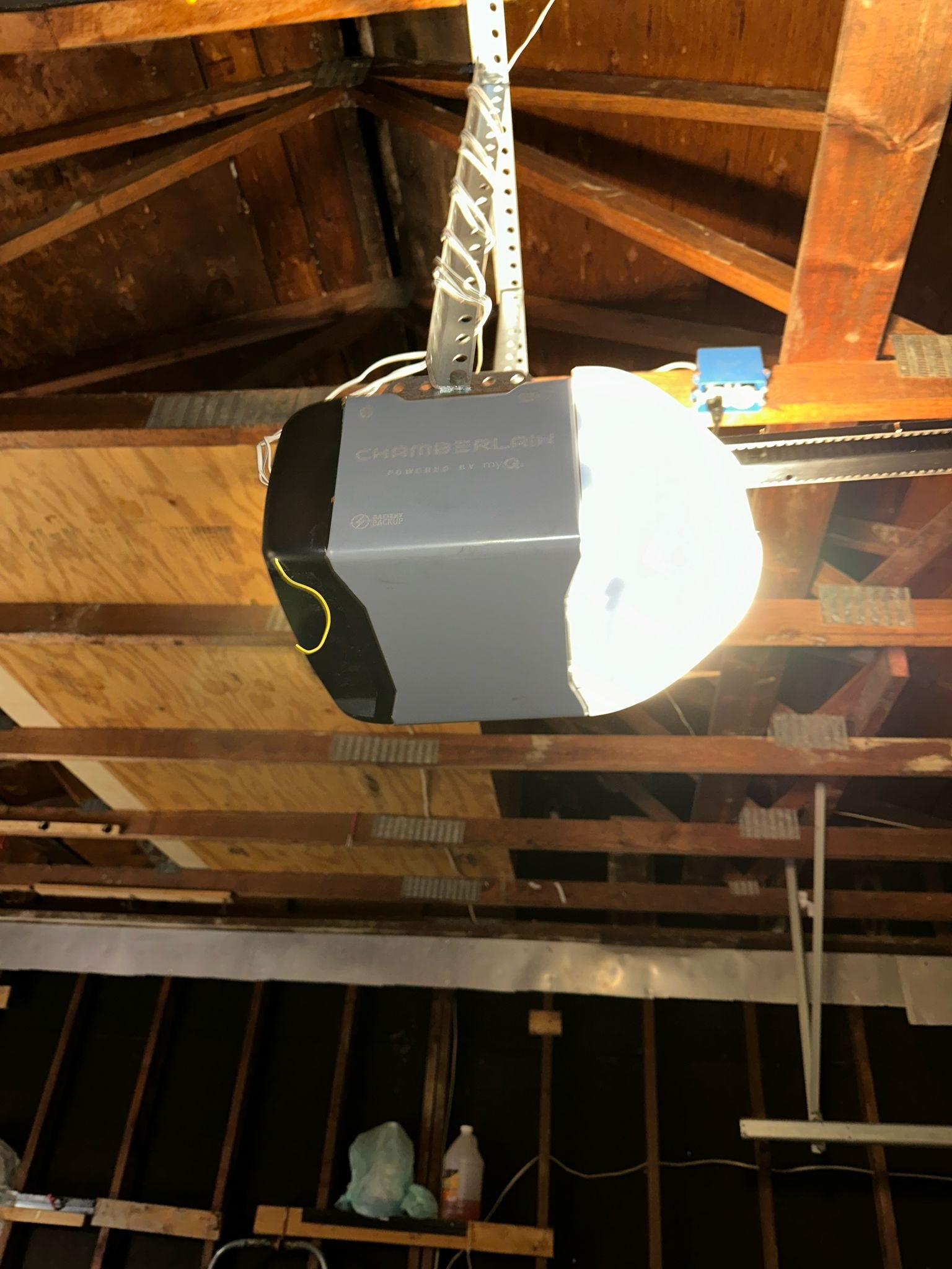 Chain-drive garage door opener mounted to exposed wood ceiling joists in a garage.