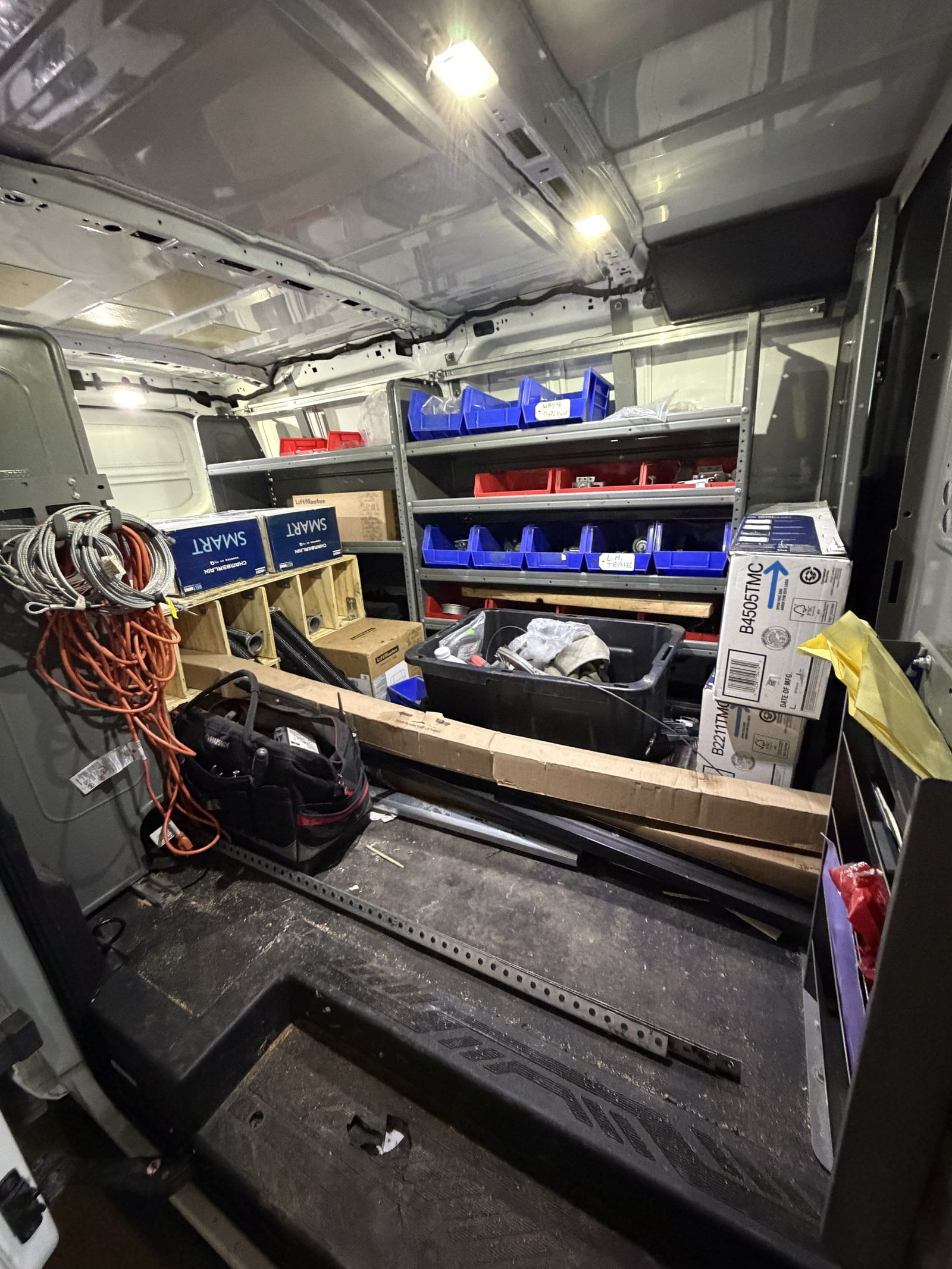 Work van interior fitted with shelving, parts bins, coiled lift cables and boxed opener units.
