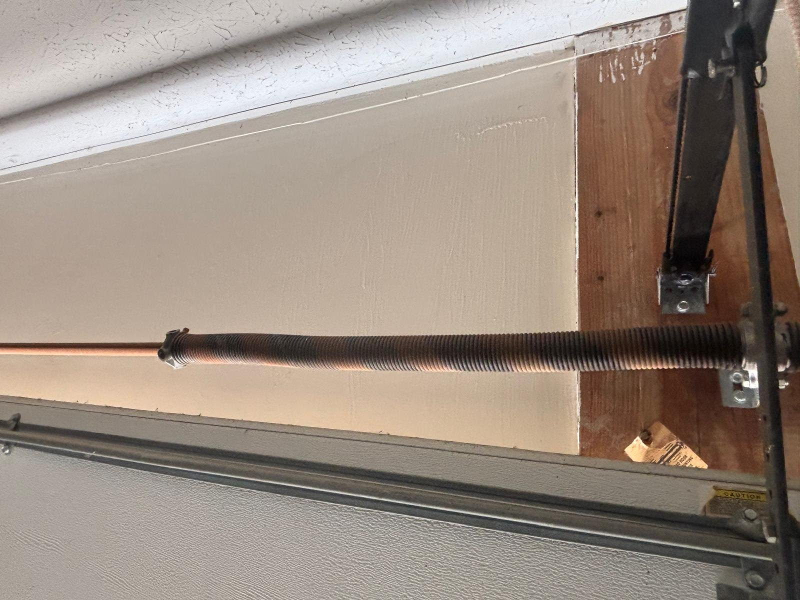 Garage door torsion spring on the shaft above the header, with the end bracket bolted to the wall.