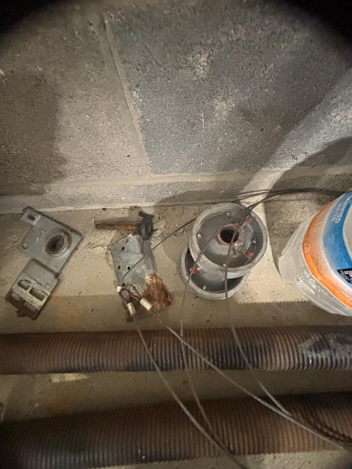 Removed garage door hardware on a concrete floor: cable drum, bearing plate, lift cables and old springs.