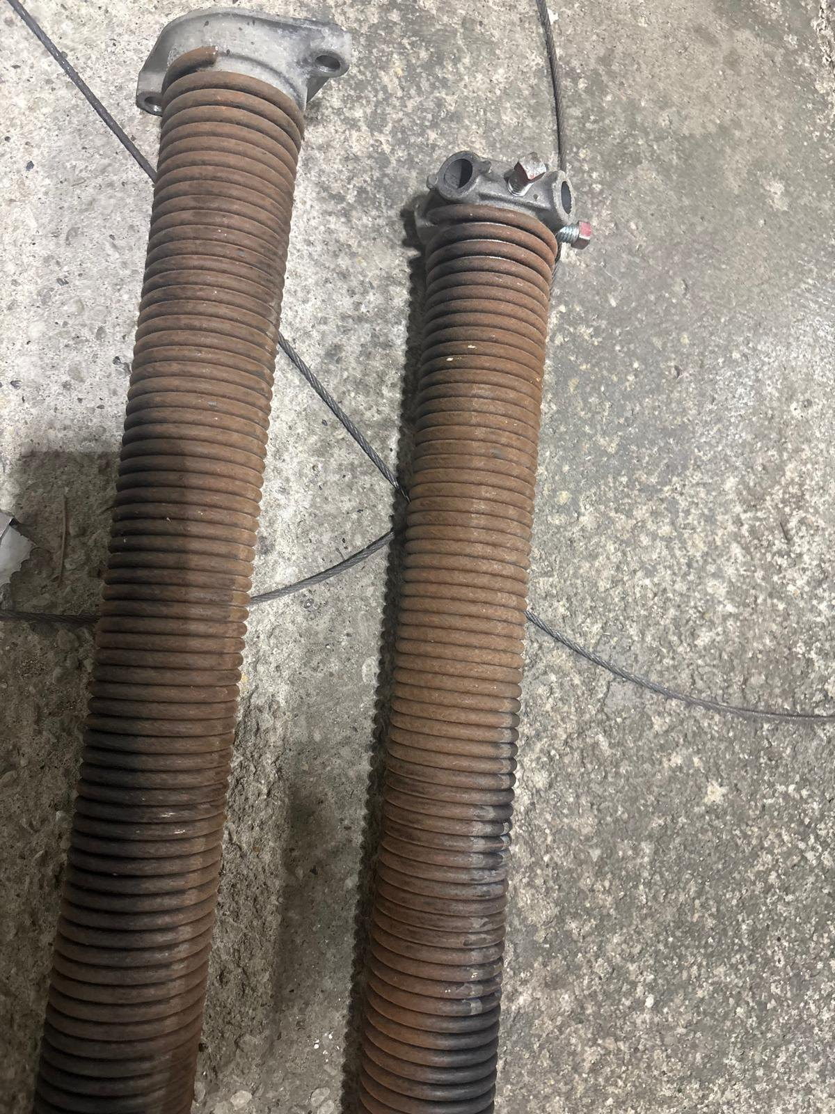 Two worn garage door torsion springs removed from a door, laid on a concrete garage floor.
