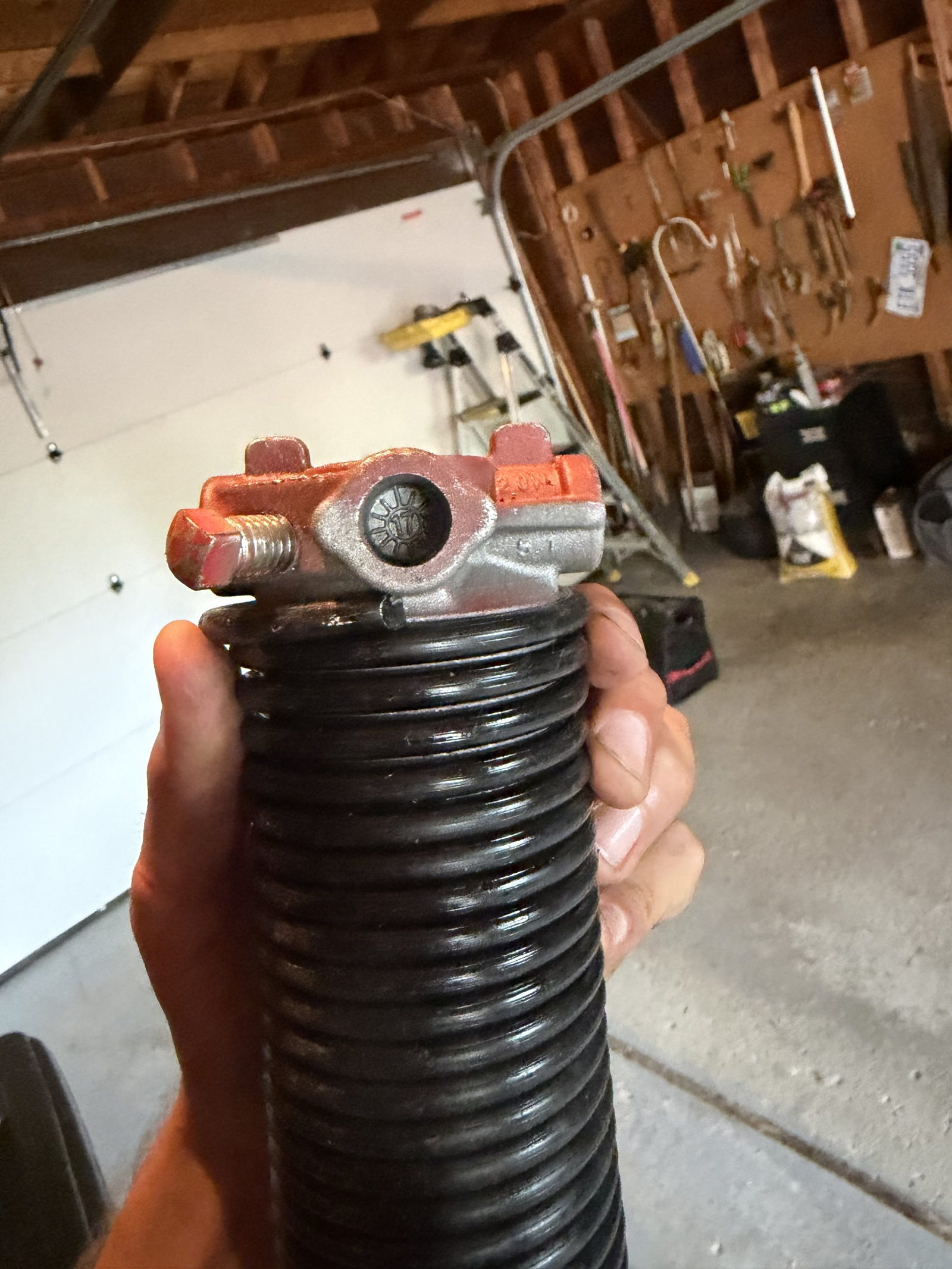 A hand holding a garage door torsion spring with its winding cone attached.